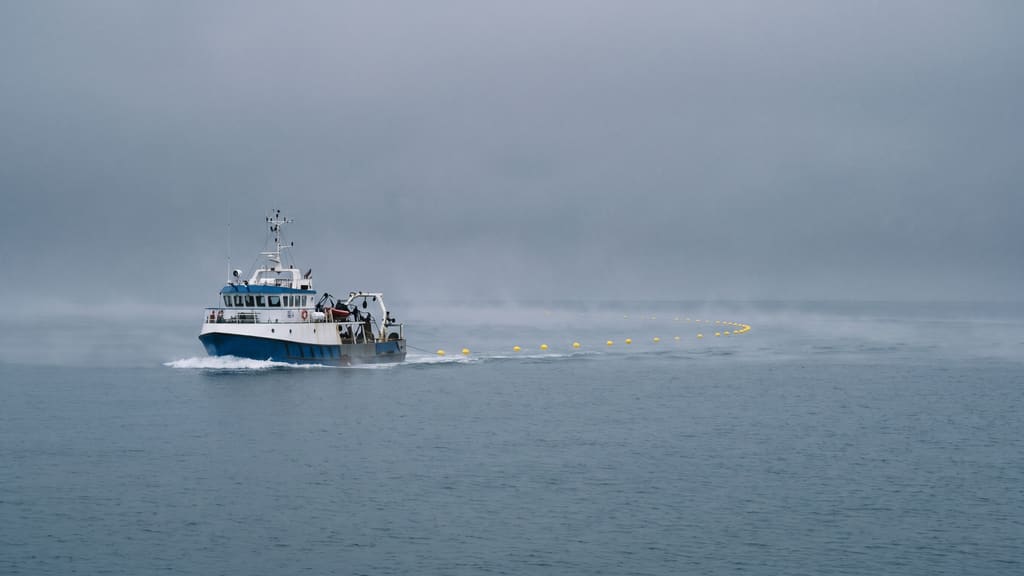 A survey boat towing a line of yellow floats along the cable corridor in flat grey weather.